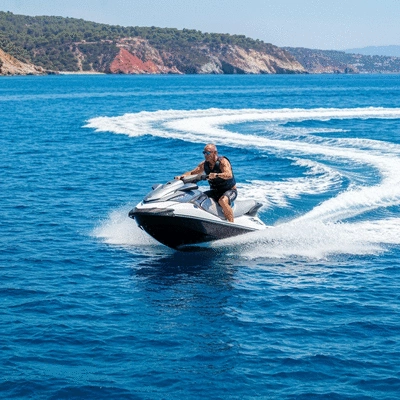 Person riding a jet ski on clear blue water with a scenic coastline in the background