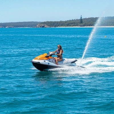 Person joyfully riding a jet ski across clear blue Australian waters with a scenic coastline in the background
